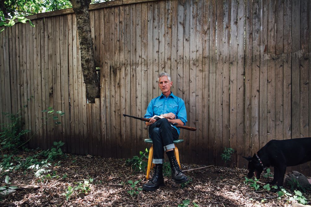 Scott Crow sitzt im Garten mit Gewehr auf den Beinen